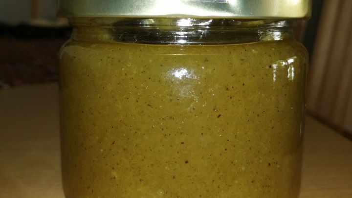 Ein Glas Rhabarbermarmelade steht auf einem Tisch und reflektiert leichtes Licht im Hintergrund einer K&uuml;che.