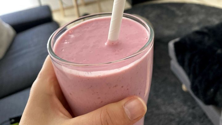Ein handgehaltener, cremiger Skyr-Himbeer-Smoothie wird mit einem Strohhalm serviert, umgeben von modernem Wohnambiente.