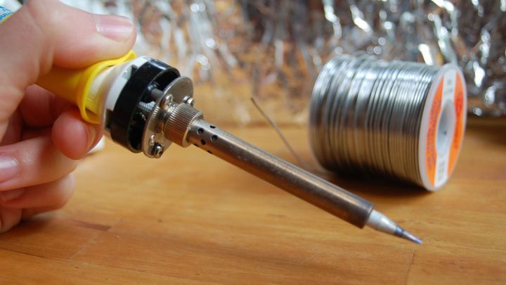 Ein L&ouml;tkolben wird gehalten, um gebrochene Kunststoffteile zu reparieren, mit einem L&ouml;tzinn-Rollen im Hintergrund.