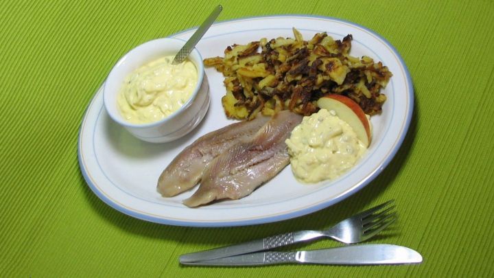 Matjesfilets liegen auf einem Teller, umgeben von krossen Kartoffelkr&uuml;meln und einer feinen So&szlig;e.