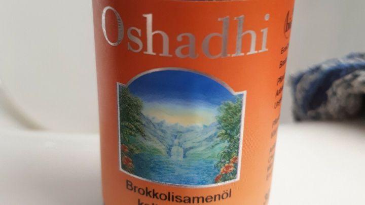 Ein blauer Glasflasche mit orangefarbigem Etikett steht auf einer Oberfl&auml;che, umgeben von Badezimmerutensilien, und zeigt &Ouml;l zum Entwirren.