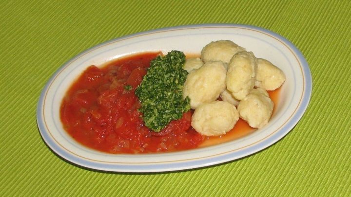 Polenta-Gnocchi liegen auf einer ovalen Platte mit Tomatenconcasse und Petersilienpesto auf einer gr&uuml;nen Tischunterlage.