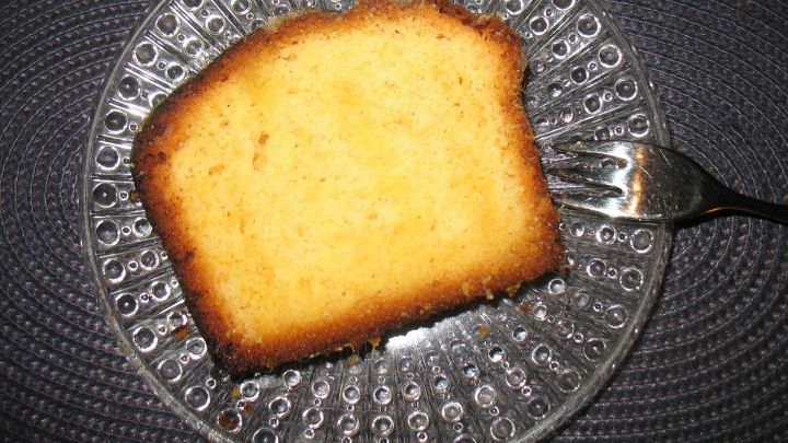 Ein St&uuml;ck saftiger Orangen-Zitronen-Kuchen liegt auf einem gl&auml;sernen Teller, w&auml;hrend eine Gabel daneben positioniert ist.