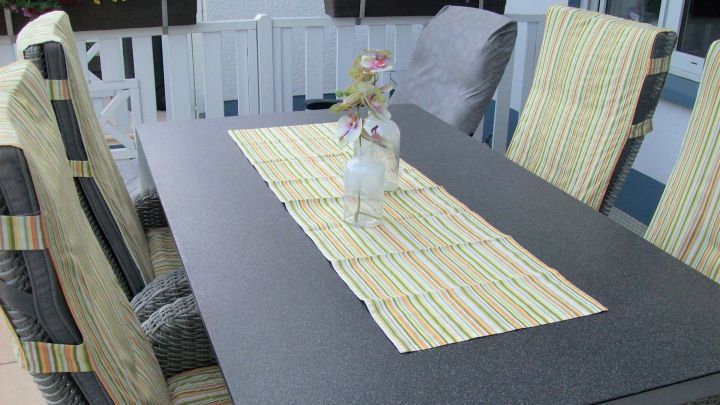 Terrassenm&ouml;bel mit bunten Sesselschonern sind um einen schwarzen Tisch angeordnet, gedeckt mit einer Tischdecke.