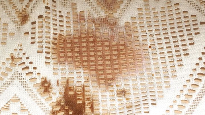 Ein helles Stoffmuster mit mehreren Blutflecken, die die Oberfl&auml;che beeintr&auml;chtigen und einen Reinigungsbedarf anzeigen.