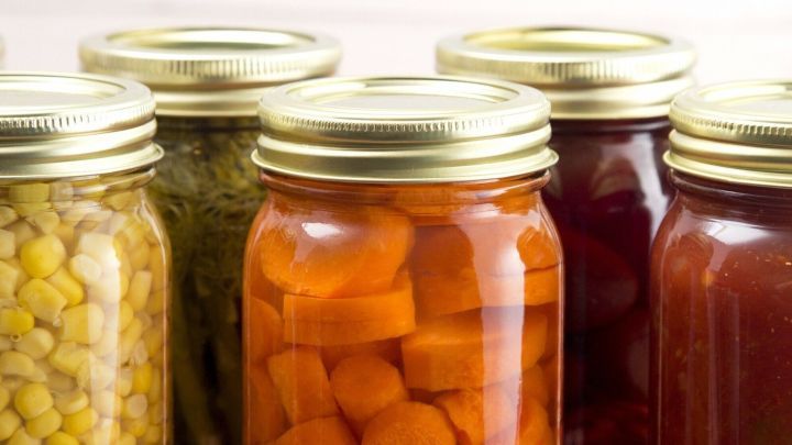 Glasbeh&auml;lter mit eingelegtem Gem&uuml;se stehen auf einem roten Karotttuch, bereit zum &Ouml;ffnen und Genie&szlig;en.