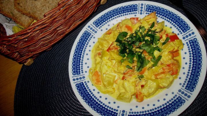 Bunte Paprika-Lauch-Curry auf einem Teller, garniert mit frischen Kr&auml;utern, neben einem Korb mit Brotscheiben.