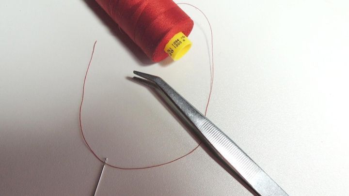 Eine rote N&auml;hgarnrolle liegt neben einer Zange, die dabei ist, den Faden einfach und schnell einzuf&auml;deln.