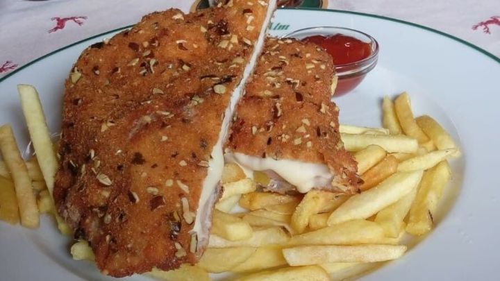 K&uuml;rbiskernschnitzel liegt auf einem Teller mit Pommes frites und einer kleinen Schale Ketchup in einem Restaurant.