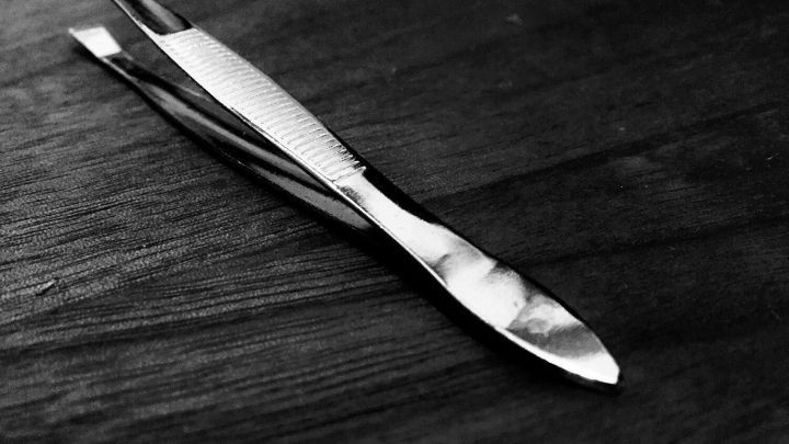 Eine gl&auml;nzende Pinzette liegt auf einem dunklen Holzuntergrund, bereit, pr&auml;zise Arbeiten durchzuf&uuml;hren.