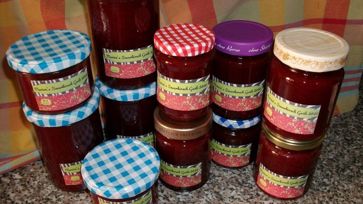 Bunte Marmeladengl&auml;ser stehen auf einer Fl&auml;che und zeigen selbstgemachte Sauerkirschmarmelade, umgeben von einem karierten Tuch.