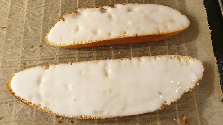 Hefegeb&auml;ck, das frisch gebacken auf einem Blech mit Backpapier liegt, zeigt verschiedene Gr&ouml;&szlig;en und einen glasierten Belag.