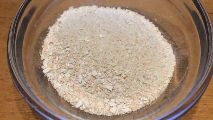 Im durchsichtigen Sch&auml;lchen befindet sich zerkleinerte Eierschale, die fein pulverisiert auf einem Holztisch liegt.