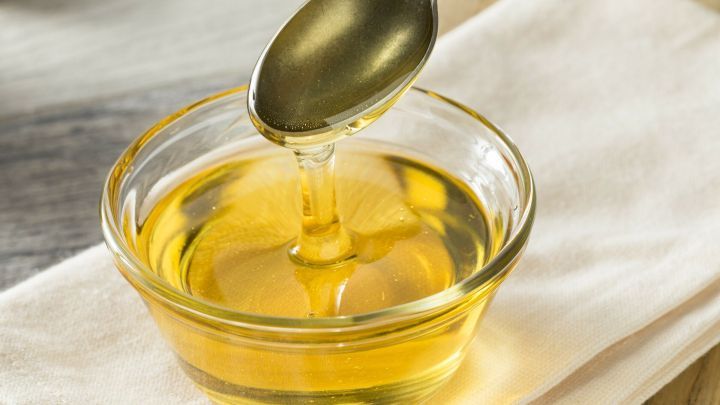 Ein L&ouml;ffel mit Agavendicksaft schwenkt &uuml;ber einer kleinen Sch&uuml;ssel, die auf einem wei&szlig;en Tuch platziert ist.