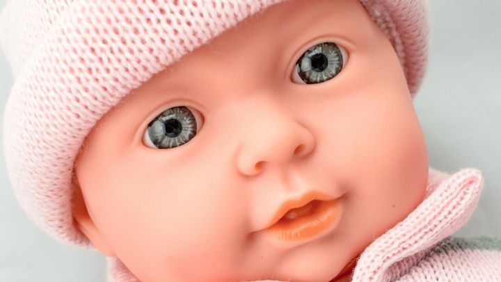 Ein Puppenkopf tr&auml;gt einen gestreiften Pullover und M&uuml;tze, w&auml;hrend er an einem hellen Untergrund platziert ist.