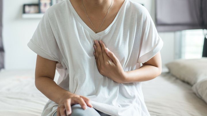 Eine Person sitzt auf einem Bett, h&auml;lt sich den Brustbereich und zeigt Anzeichen von Unbehagen aufgrund von Sodbrennen.