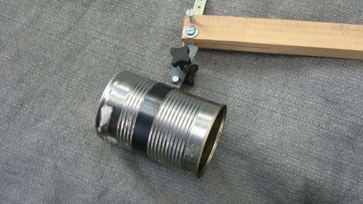 Ein metallischer Eimer h&auml;ngt an einem Holzarm und wird zur Reinigung der Regenrinne verwendet. Die Umgebung ist grau und neutral.