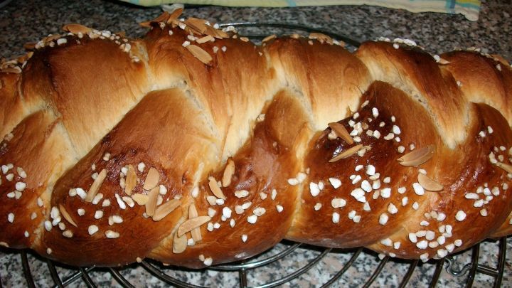 Ein goldbrauner Hefezopf mit Anis liegt auf einem Gitter, bestreut mit grobem Zucker und Mandeln, im K&uuml;chenumfeld.