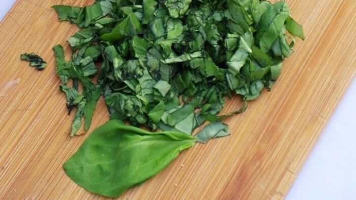 Frischer, gehackter Basilikum liegt auf einem Holzbrett, bereit zur Verwendung in Rezepten gegen trockene und juckende Kopfhaut.