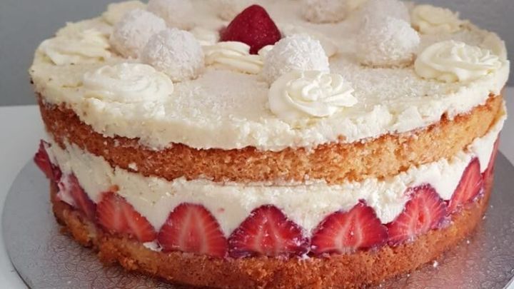 Eine saftige Raffaellotorte mit Erdbeeren steht auf einem silbernen Teller, umgeben von einer neutralen Wand und sorgt f&uuml;r einen ansprechenden Anblick.