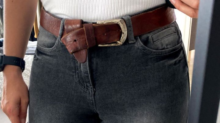 Ein brauner G&uuml;rtel ist um die Taille einer Person gebunden, die enge Jeans tr&auml;gt. Der Hintergrund zeigt einen Spiegel und einen hellen Boden.