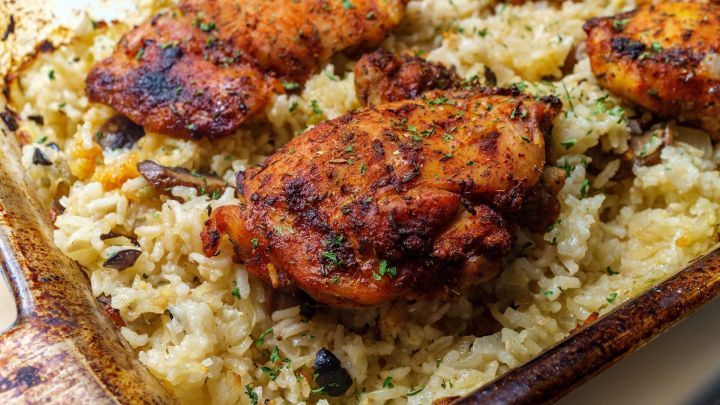 H&auml;hnchenschenkel liegen gebr&auml;unt auf einem Bett aus duftendem Reis und Kr&auml;utern in einer Auflaufform.