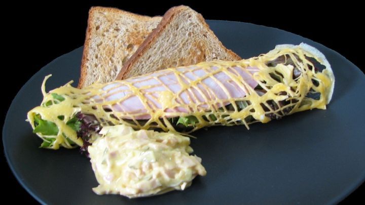 Ein gef&uuml;lltes Spitzendeckchen auf einem schwarzen Teller, umgeben von zwei Toastscheiben und Salat, serviert mit Salatcreme.