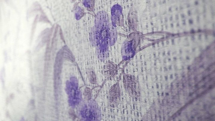 Ein Fettfleck auf der Tapete zeigt lila Blumenmuster auf strukturierter Oberfl&auml;che in einem hellen Raum.