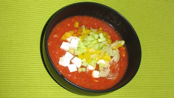 Eine Sch&uuml;ssel Gazpacho pr&auml;sentiert eine leuchtend rote Suppe, garniert mit frischem Gem&uuml;se auf einem gr&uuml;nen Untergrund.