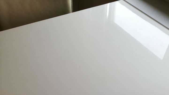 Ein heller Hochglanztisch reflektiert Licht, w&auml;hrend er auf einer glatten Oberfl&auml;che steht, die sauber und modern wirkt.