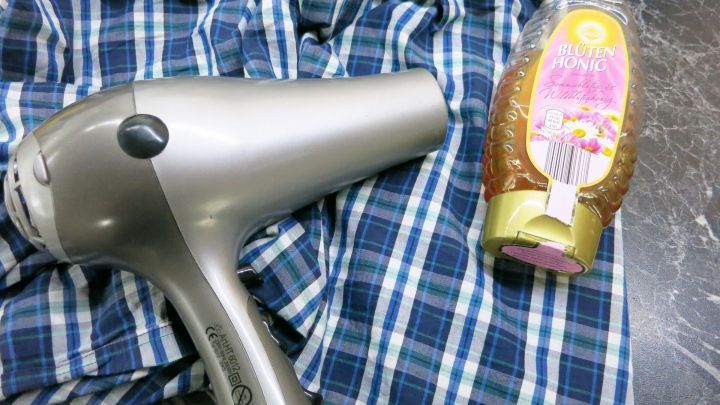 Ein Haartrockner liegt auf einem karierten Tuch neben einem Honigglas, das f&uuml;r das Entfernen von Superkleber genutzt wird.