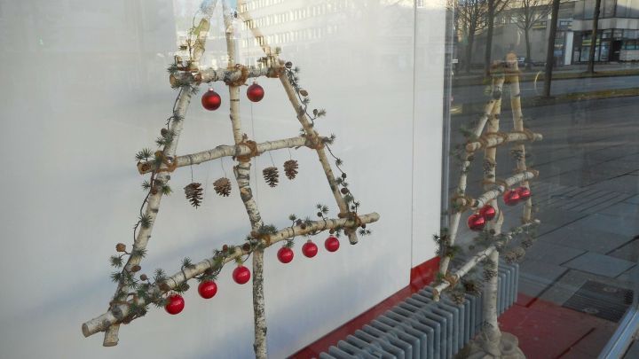 Ein dekorativer Christbaum aus Naturmaterialien steht vor einem Fenster, geschm&uuml;ckt mit roten Kugeln.