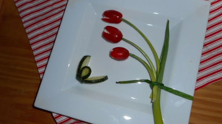 Rote Tomatentulpen stehen auf einem wei&szlig;en Teller, umgeben von einem gr&uuml;nen Schnittlauchst&auml;ngel, auf gestreiftem Untergrund.