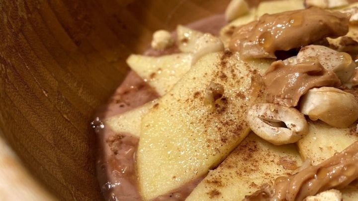Eine Holzsch&uuml;ssel mit kalorienarmen Pudding-Oats, garniert mit Apfelst&uuml;cken, N&uuml;ssen und Zimt, sieht einladend aus.