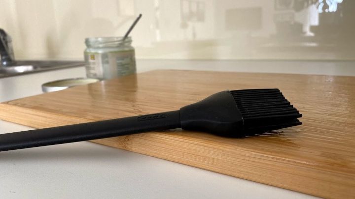 Ein Holz-Schneidebrett liegt auf einem Tisch, w&auml;hrend ein Pinsel darauf abgest&uuml;tzt wird, um es zu pflegen.