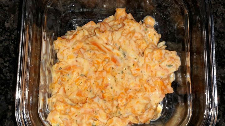 Ein cremiger veganer Gem&uuml;seaufstrich wird in einer Glasbeh&auml;lter pr&auml;sentiert, auf einer dunklen Arbeitsfl&auml;che.