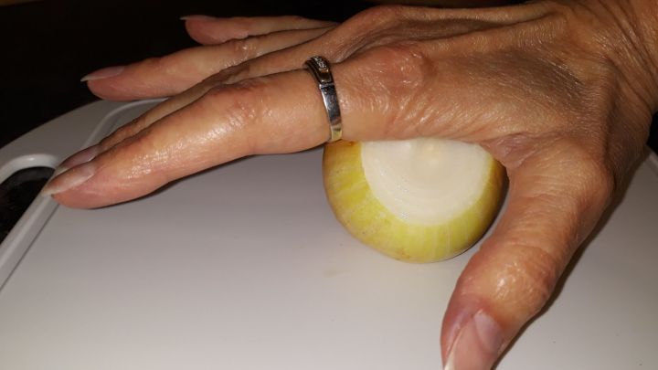 Eine Hand h&auml;lt eine gesch&auml;lte Zwiebel auf einem Schneidebrett, w&auml;hrend eine Klinge zum Schneiden bereit ist.