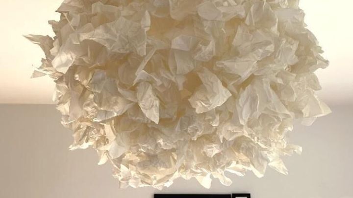 Ein schwebender Ikea-Regolit-Lampenschirm, kunstvoll mit Butterbrotpapier dekoriert, in einem hellen Raum mit Rahmenbildern.