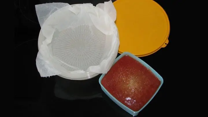 Die Tomatensoße soll sehr langsam auftauen. Dafür ein Sieb mit einem nass gemachten Küchenkrepp auslegen und so in / über eine Schüssel hängen, dass etwa ein halber Liter Flüssigkeit darunter passt.