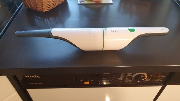 Ein Handstaubsauger liegt auf einer dunklen Tischplatte, bereit, Spinnweben von der Decke zu entfernen.