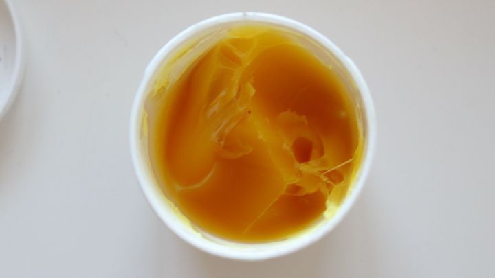 Ein runder Beh&auml;lter mit gelbem Wollfett steht auf einer glatten Oberfl&auml;che, bereit zur sanften Entfernung von H&uuml;hneraugen.