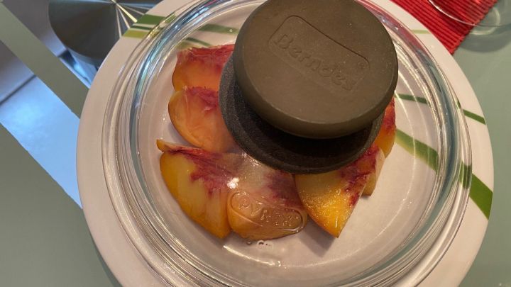 Geschnittenes Obst liegt unter einem Topfdeckel auf einem Teller, um es frisch zu halten. Der Tisch hat eine moderne Oberfl&auml;che.