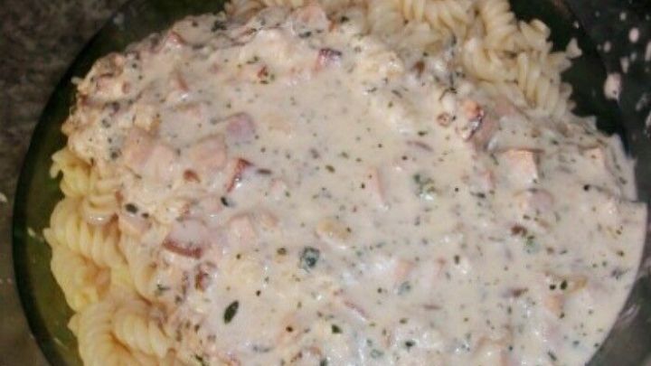 Cremige K&auml;se-Sahne-So&szlig;e umgeben Spiralnudeln in einer Sch&uuml;ssel auf einer dunklen Arbeitsplatte.