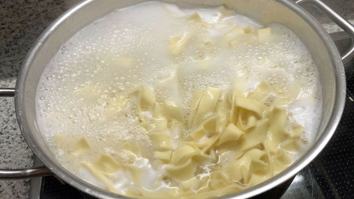 Ein Topf mit kochenden Nudeln sprudelt auf dem Herd, umgeben von einer modernen K&uuml;chensituation.