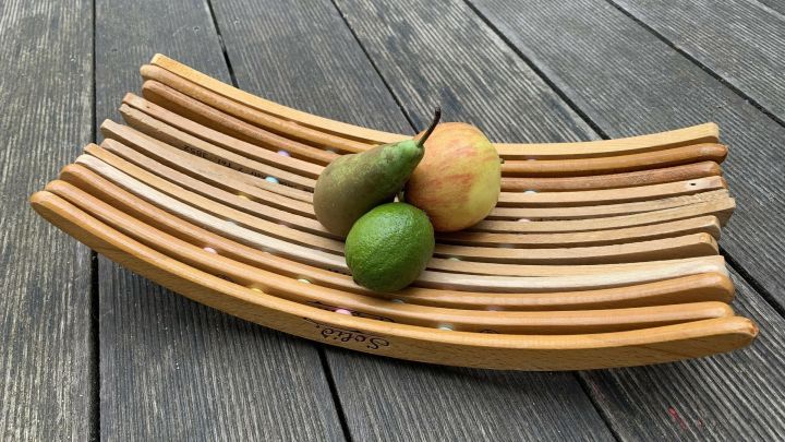 Eine Obstschale aus alten Holzb&uuml;geln steht auf einem Holztisch, dekoriert mit einer Apfel-, Birnen- und Limone.