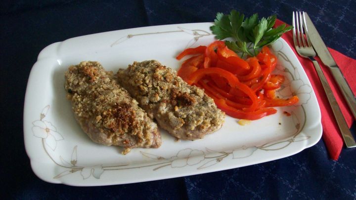 Zwei knusprige Kalbsschnitzel liegen auf einem wei&szlig;en Teller, umgeben von frischem Paprikagem&uuml;se und Petersilie.