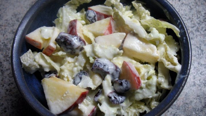 Ein frischer Chinakohl-Salat mit Apfel und Cranberrys liegt in einer Sch&uuml;ssel, umgeben von einer mottierten Oberfl&auml;che.