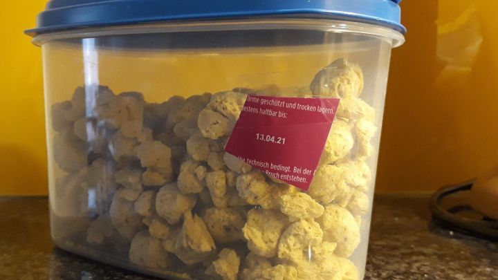 Ein durchsichtiger Vorratsbeh&auml;lter steht auf einer Granitabdeckung. Er enth&auml;lt gelbe Snacks und hat ein etikettiertes Haltbarkeitsdatum.