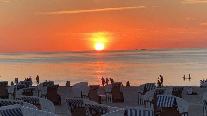 Strandk&ouml;rbe stehen am Ostseestrand, w&auml;hrend die Sonne orange leuchtet und eine ruhige Abendstimmung erzeugt.