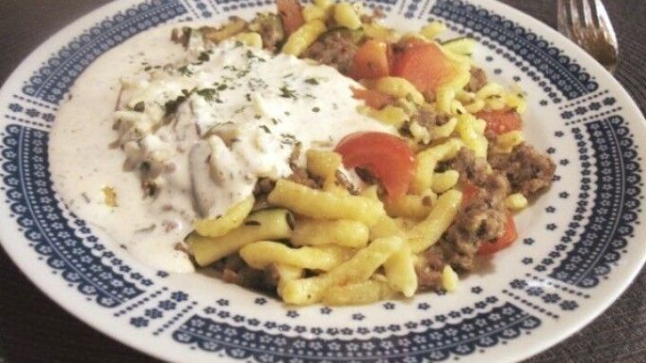 Eine dampfende Portion w&uuml;rzige Hack-Zucchini-Pfanne mit Sp&auml;tzle und Kr&auml;uterschmand ist auf einem dekorativen Teller angerichtet.